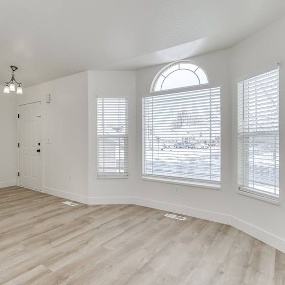 a room with wooden floors and white walls, featuring a staircase, a door, and a window with blinds.