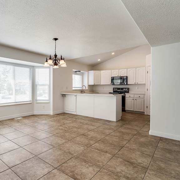 an empty kitchen with a chandelier and a door to the living room