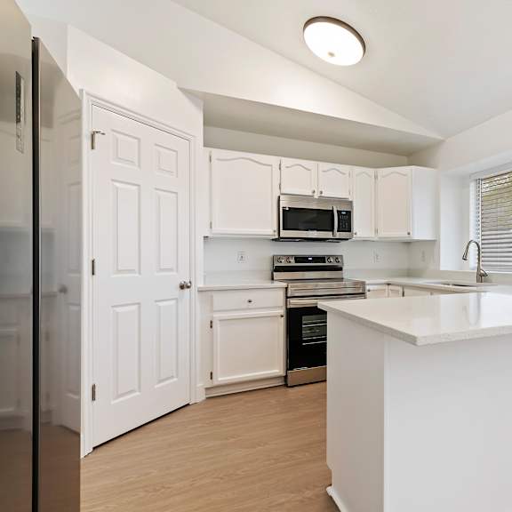 a white kitchen with a refrigerator, oven, microwave, and cabinets.