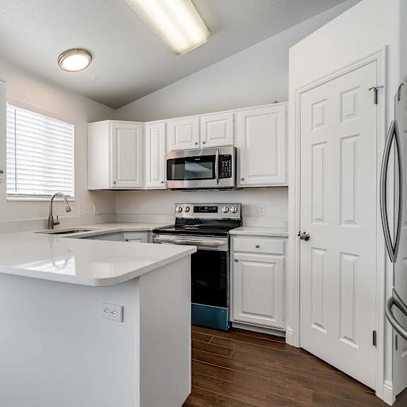 a white kitchen with a refrigerator, microwave, oven, and sink.