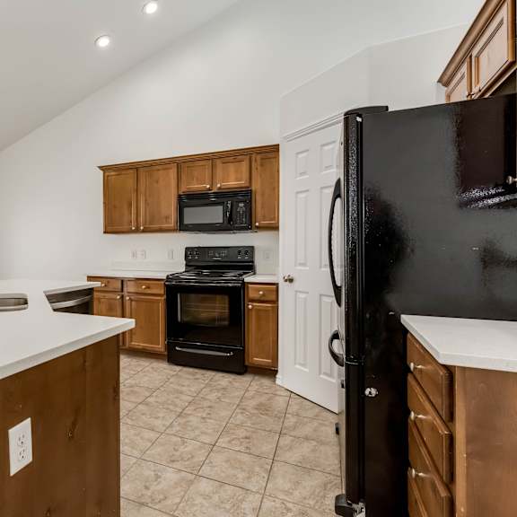 a kitchen with a black refrigerator, wooden cabinets, and a white countertop.