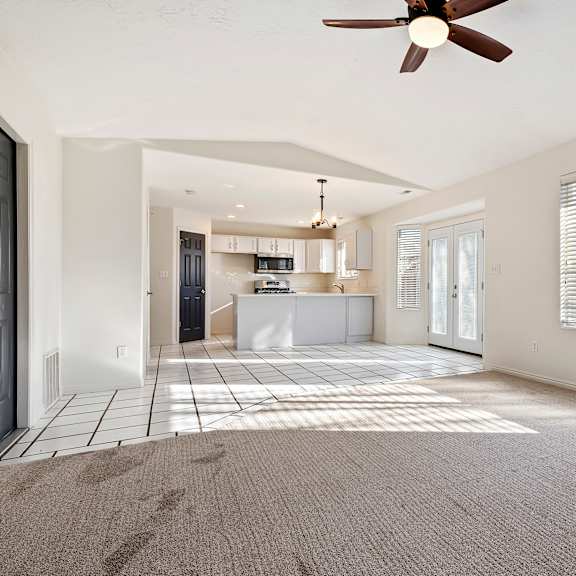 an empty living room with a ceiling fan and a kitchen