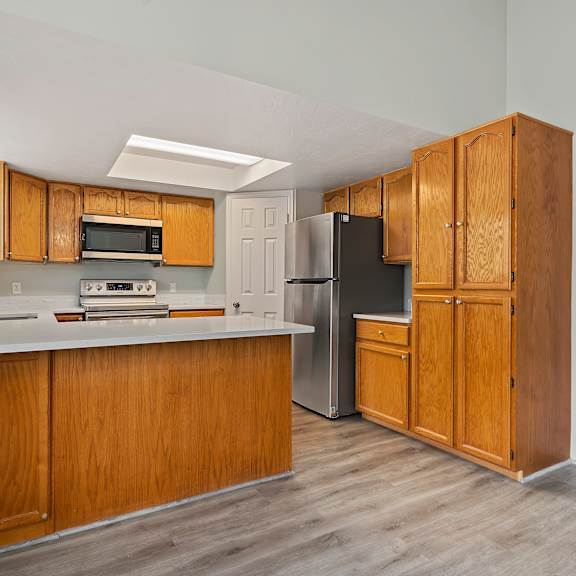 an empty kitchen with wooden cabinets and a stainless steel refrigerator