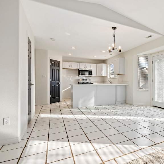 an open kitchen and living room with white cabinets and tiled flooring