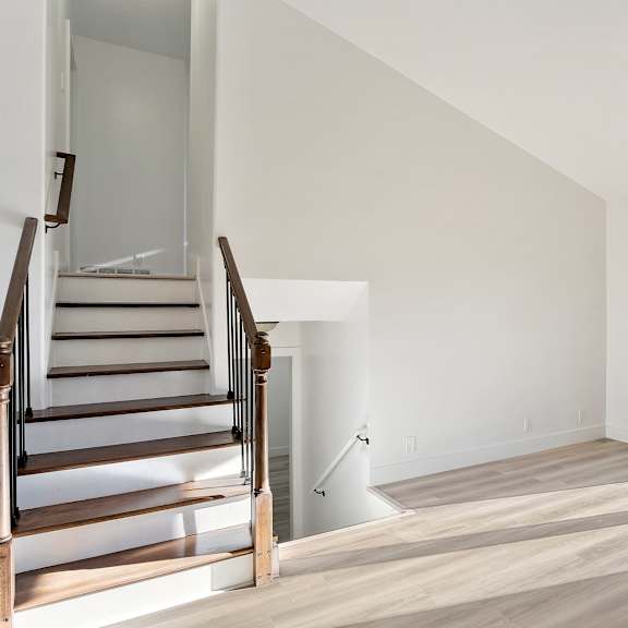 a living room with white walls and a staircase and a glass door