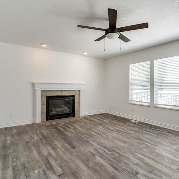 an empty living room with a fireplace and a ceiling fan