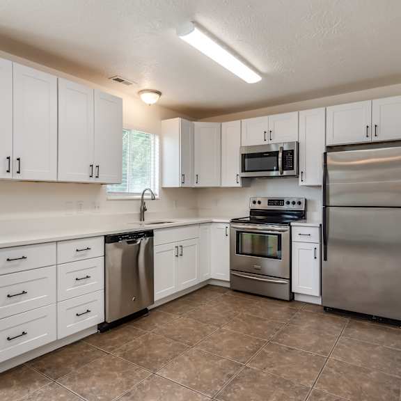 an empty kitchen with stainless steel appliances and white cabinets