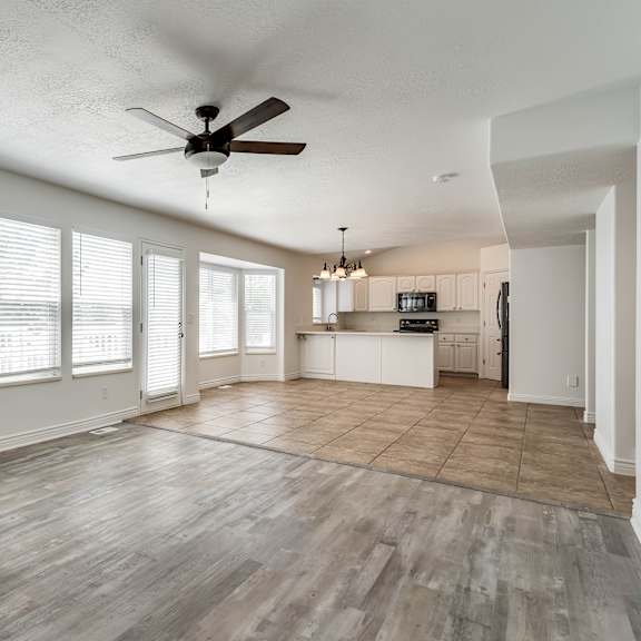 an empty living room with a ceiling fan and a kitchen