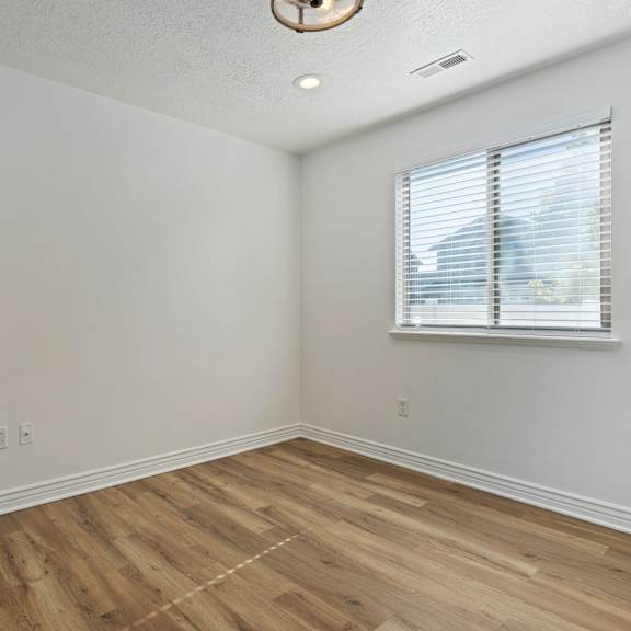 a room with wooden flooring and a window with blinds.