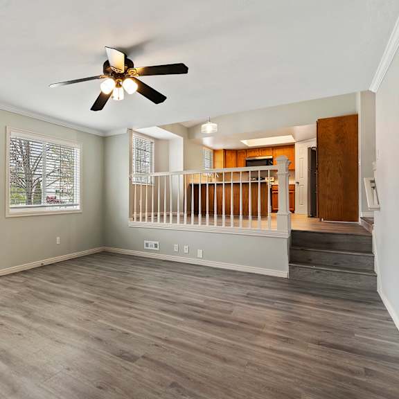 an empty living room with a ceiling fan and a staircase