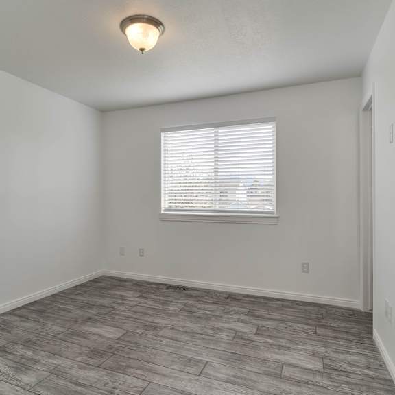 a room with a window covered by white blinds and a light grey floor.