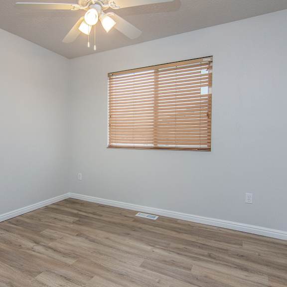 an empty room with wooden floors and a window and a ceiling fan