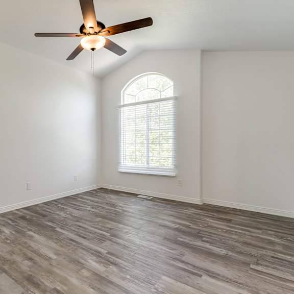 an empty living room with a ceiling fan and a window
