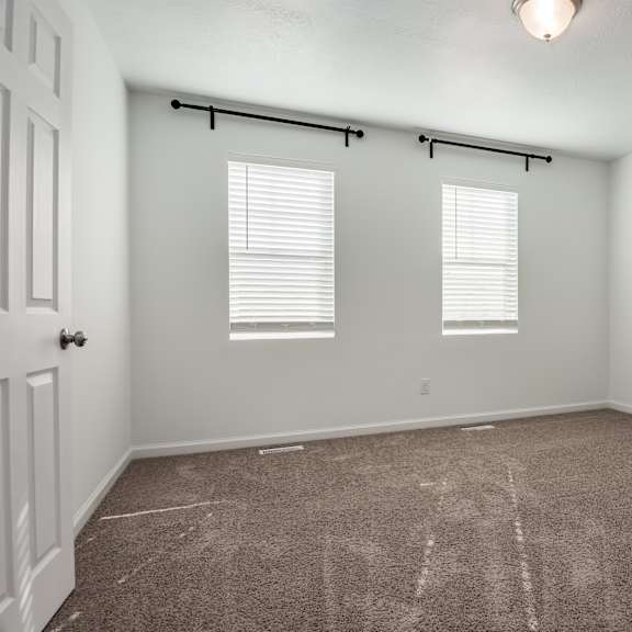 a room with a carpeted floor and two windows with blinds.