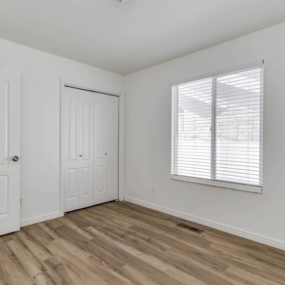a bedroom with white walls and wood floors and a window