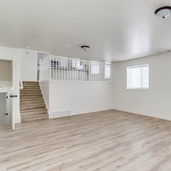 a spacious room with wooden floors and a staircase leading to another level.