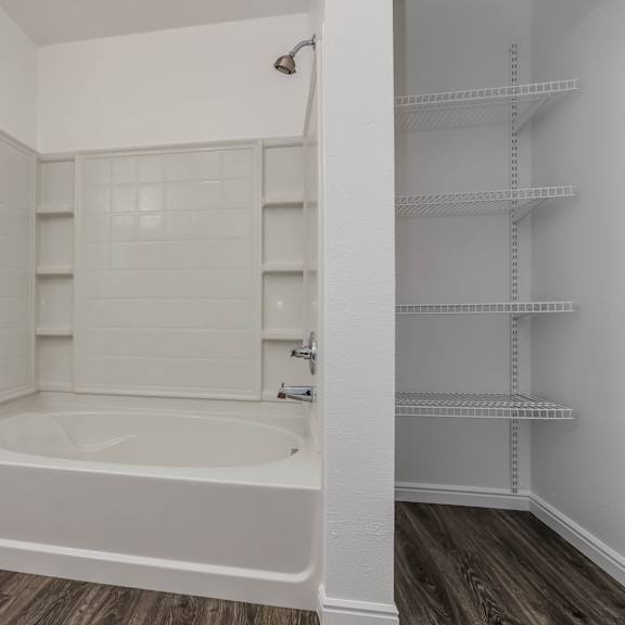 a white bathroom with a tub and shelves.