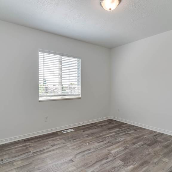 the living room of an empty home with wood flooring and a window