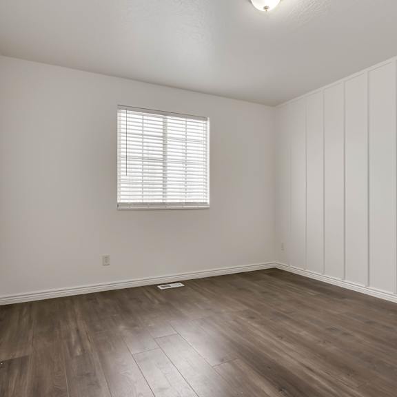 a room with wooden flooring and a window with blinds.