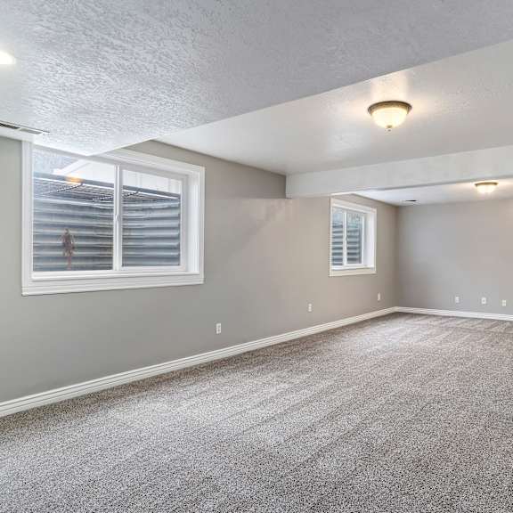 a spacious room with grey carpeting and two windows.