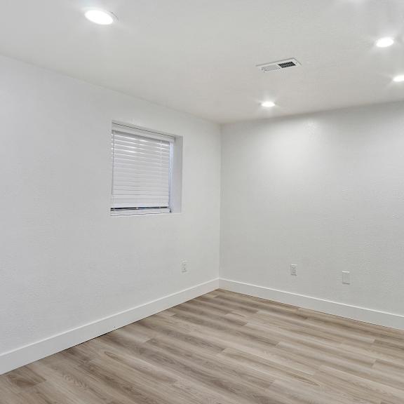 a bedroom with white walls and wood flooring and a window