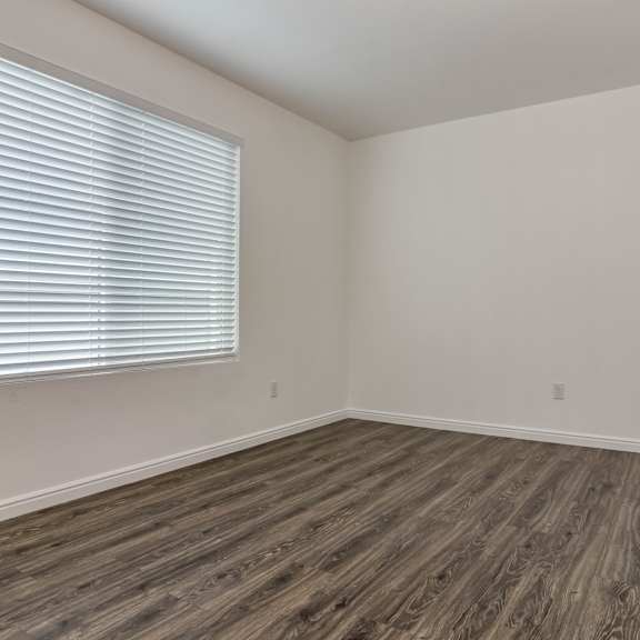 a room with wooden flooring and a window with blinds.