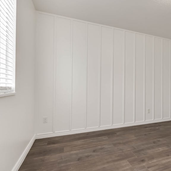a room with wooden flooring and white walls with a door on the right.