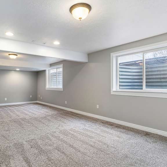 a spacious room with grey carpeting and a window with blinds.