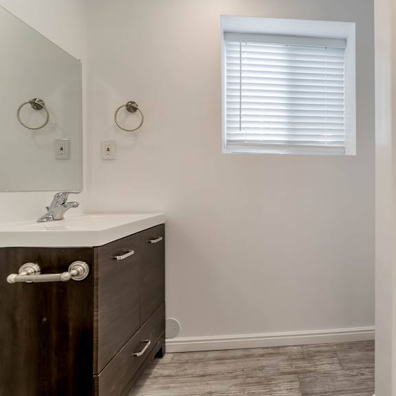 a bathroom with a sink, mirror, and a window with blinds.