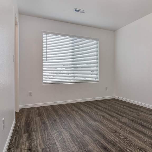 a room with a window covered by white blinds and wooden flooring.