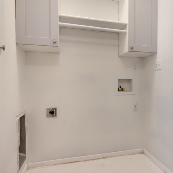 a laundry room with white walls and white cabinets and a hole in the wall