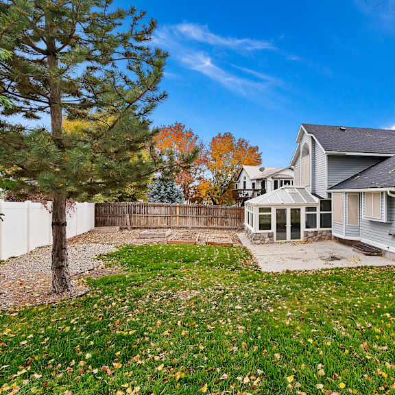 a house with a grey roof and a white fence is surrounded by a grassy area with fallen leaves.