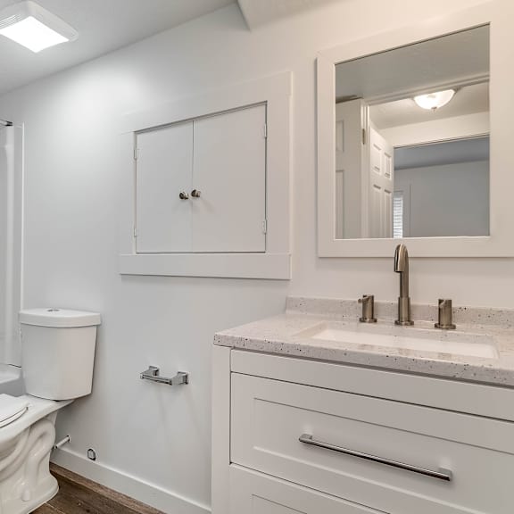a white bathroom with a toilet, sink, and mirror.