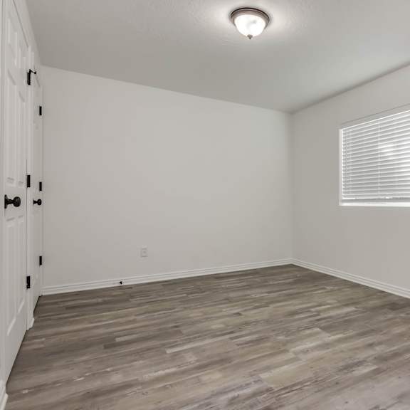 a room with wooden flooring and a window with blinds.