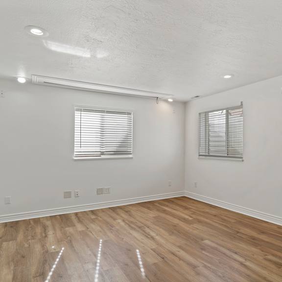 a room with wooden floors and two windows with blinds.