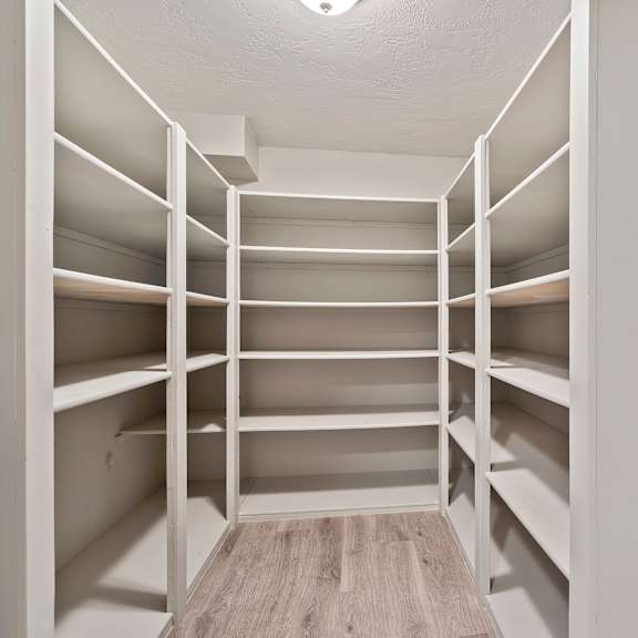 a large walk in closet with white shelves and a wooden floor