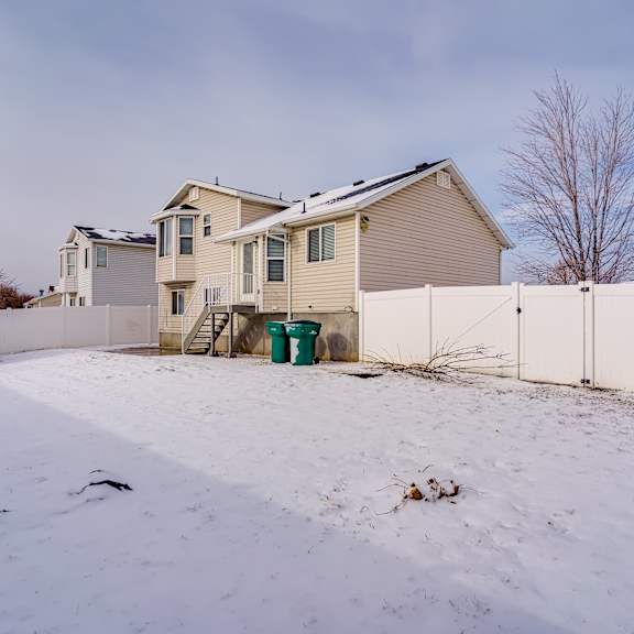 a house with a white fence and a green trash can in the snow.
