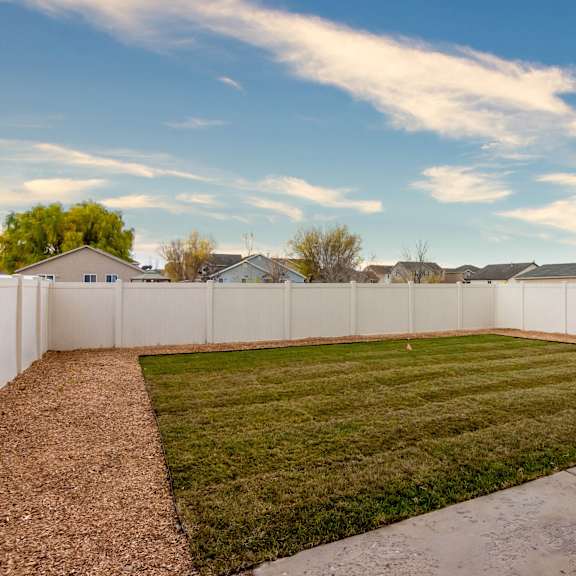 a backyard with a white fence and a green lawn.