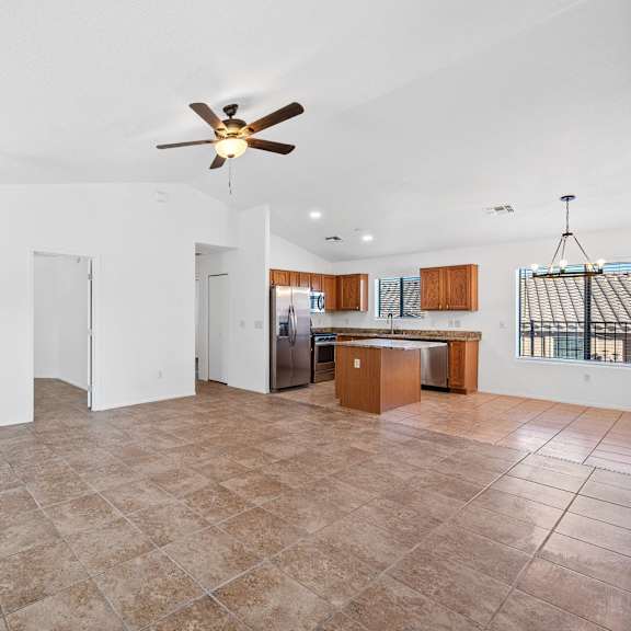 an empty living room with a ceiling fan and a kitchen
