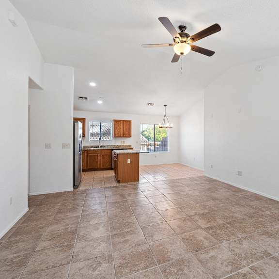 an empty living room with a ceiling fan and a kitchen