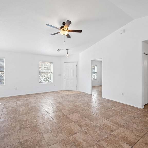 an empty living room with a ceiling fan and tiled floors
