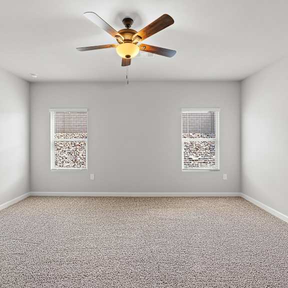 a room with a ceiling fan and two windows with curtains.