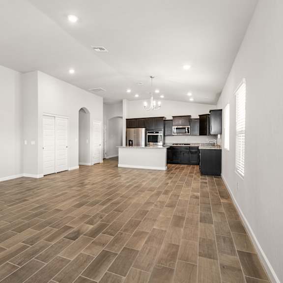 a spacious room with wooden flooring and a kitchen area in the background.