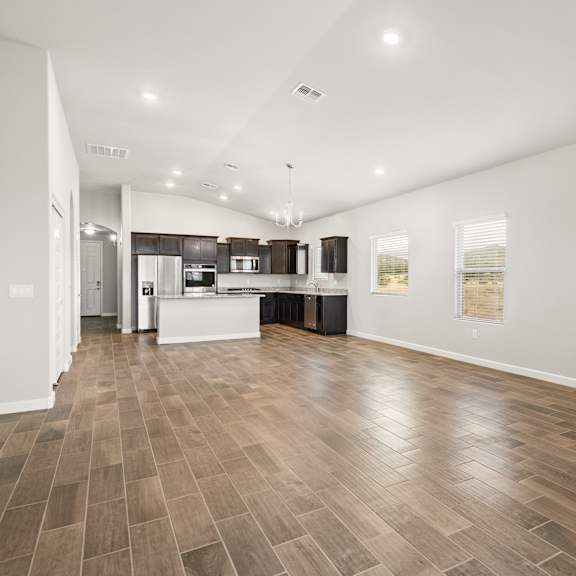 a spacious room with wooden flooring and a kitchen area in the background.