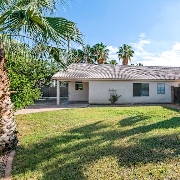 a house with a white exterior and a brown roof is surrounded by palm trees.