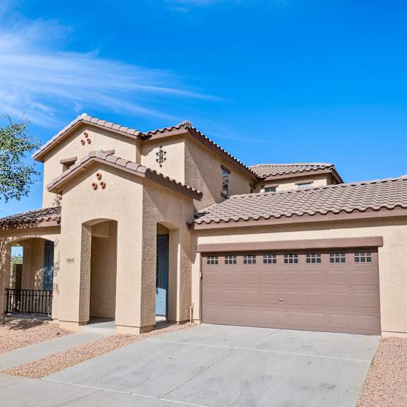 a house with a brown roof and tan walls has a garage door and a driveway.