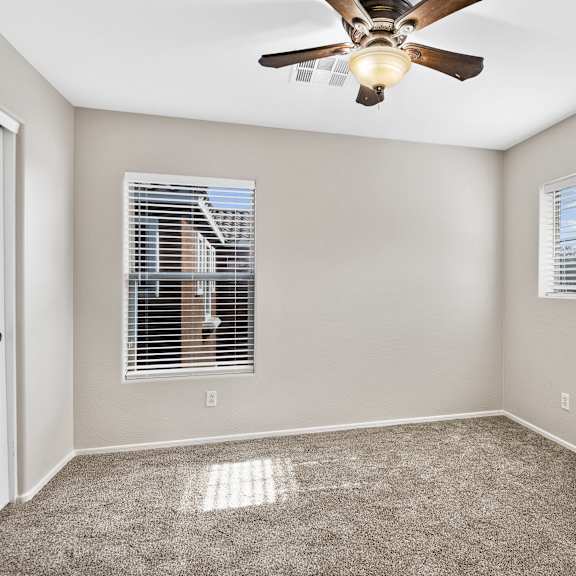 a room with a ceiling fan and two windows.