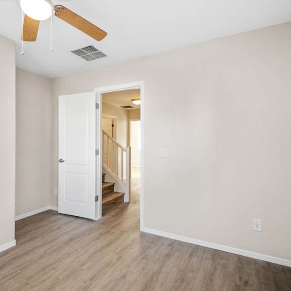 an empty living room with a ceiling fan and a door to a staircase