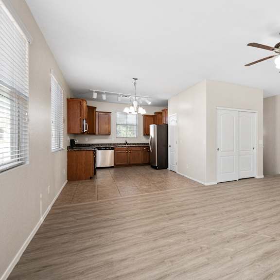 an empty living room with a ceiling fan and a kitchen