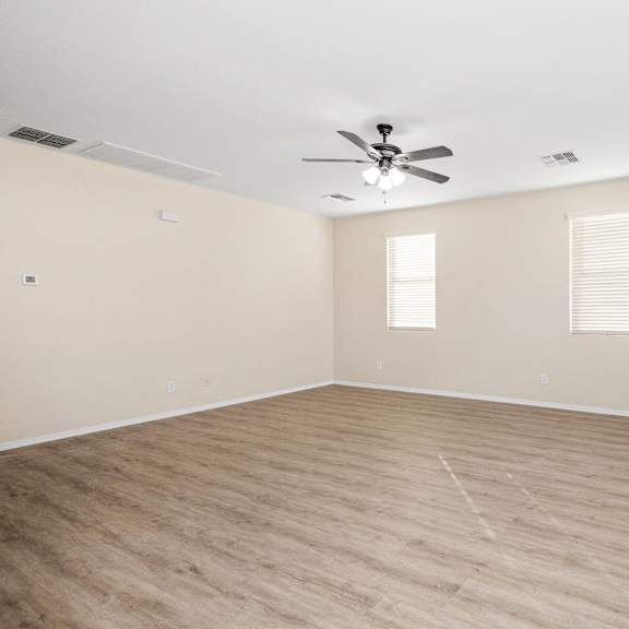an empty living room with a ceiling fan and windows
